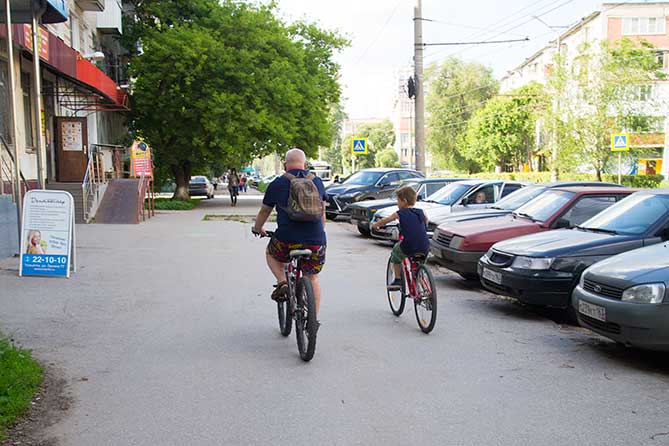 отец с сыном едут на велосипедах по тротуару