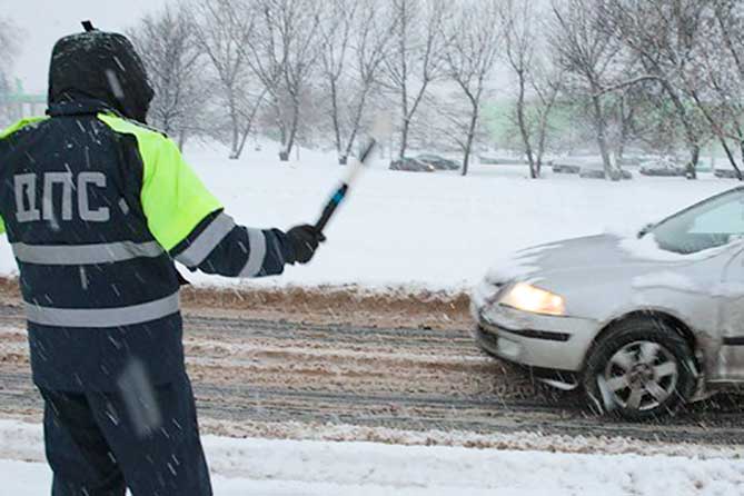сотрудник ГИБДД останавливает автомобиль на дороге зимой
