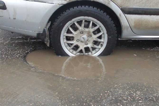колесо автомобиля в яме на дороге