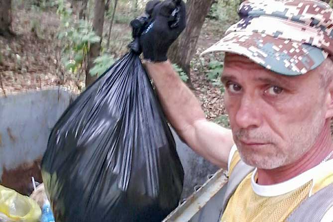 мужчина с мешком мусора возле контейнера