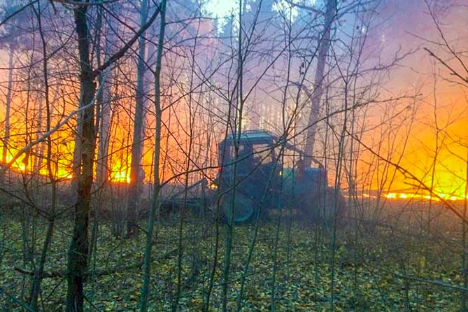 трактор вспахивает землю от огня