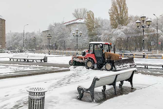 трактор убирает снего на тротуаре возле филармонии