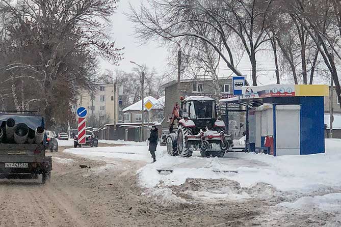 трактор расчищает снег на останвке по улице Карла Маркса