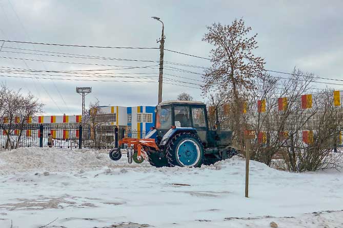 трактор чистит снег на аллее на улице Карла Маркса