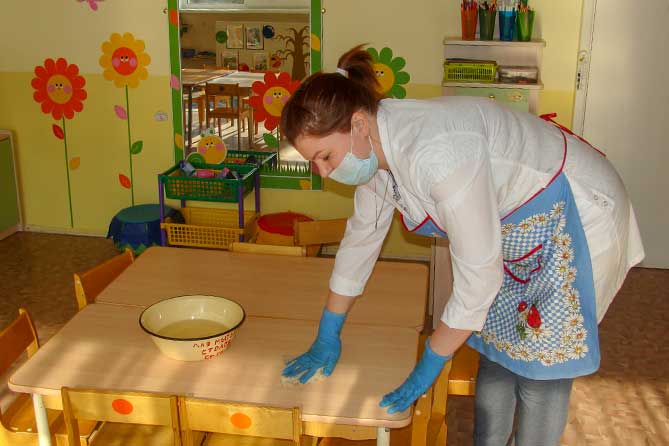 женщина вытирает стол в детском саду