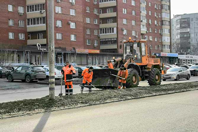 работники убирают грязь возле бордюров