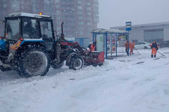 трактор чистит снег на остановке