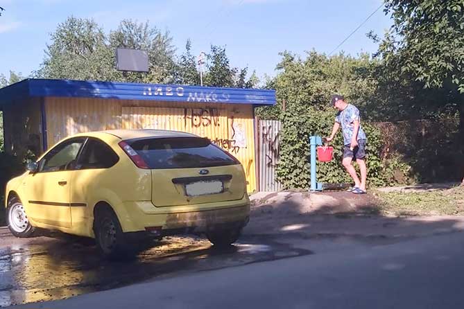 мужчина набирает воду из колонки для мытья машины