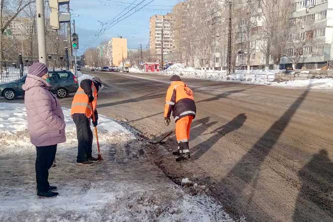 дорожные рабочие чистят снег у пешеходного перехода