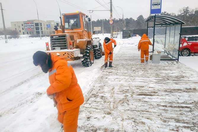 работники дорожной службы чистят снег на остановке