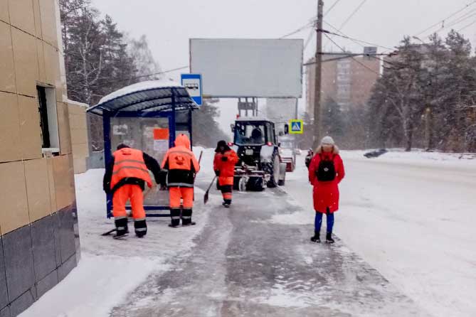 рабочие чистят снег на остановочном пункте