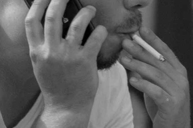 мужчина с сигаретой разговаривает по сотовому телефону