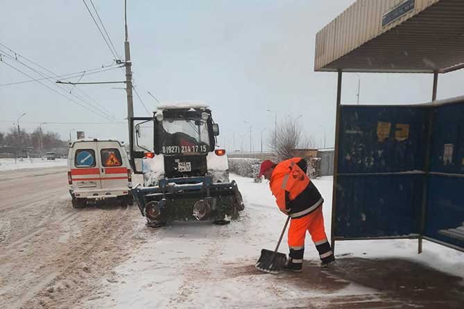 работник дорожной службы чистит снег на остановке
