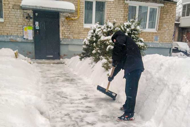 дворник чистит снег возле подъезда