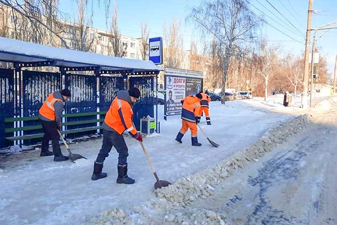 дорожные рабочие очищают остановку от снега