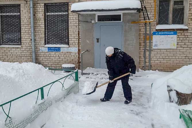 дворник чистит снег у подъезда