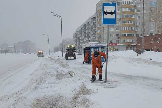 дорожные рабочие убирают снег на остановке