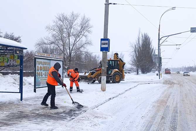 дорожные рабочие и техника чистят снег на остановке