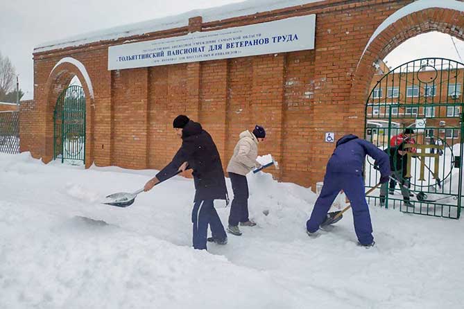 сотрудники администрации убирают снег возле пансионата для ветеранов