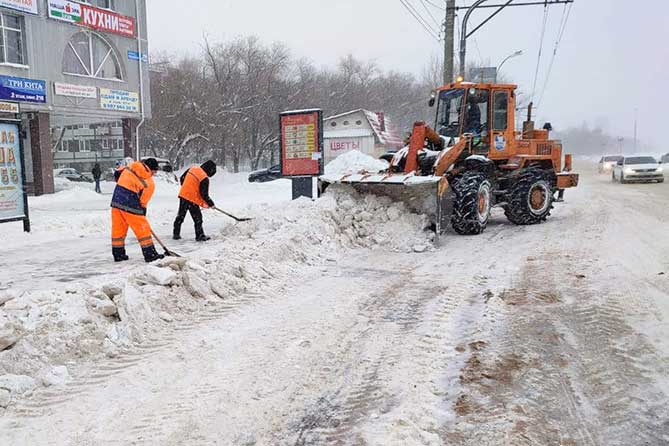 дорожные рабочие и трактор расчищают дорогу от снега