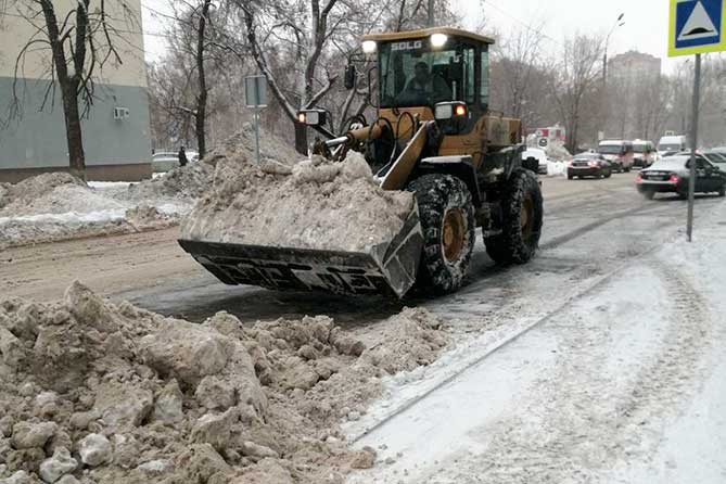 трактор чистит снег на дороге днем