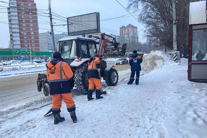 трактор чистит снег на остановке на улице Мира