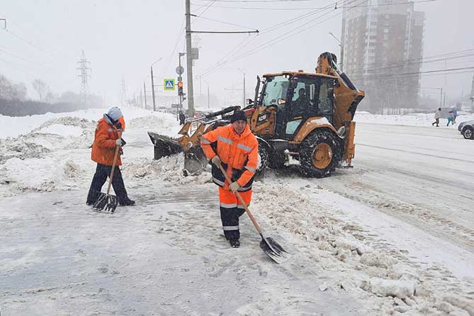 дорожные рабочие расчищают снег на остановке