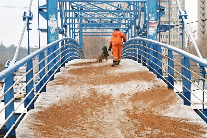 дорожный рабочий рассыпает песок на мосту