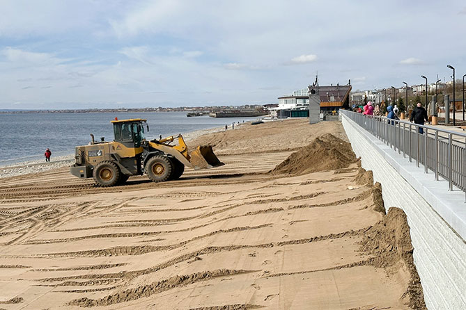 трактор разравнивает песок на пляже набережной