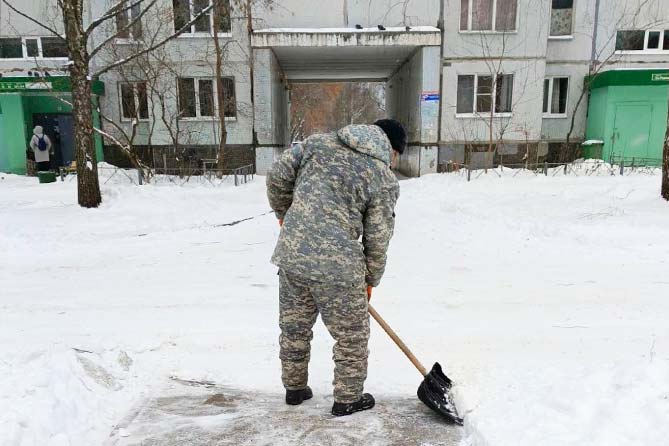 дворник расчищает снег во дворе