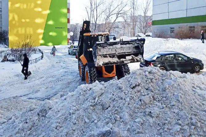 трактор сгребает снег во дворе