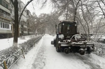 трактор убирает снег на тротуаре