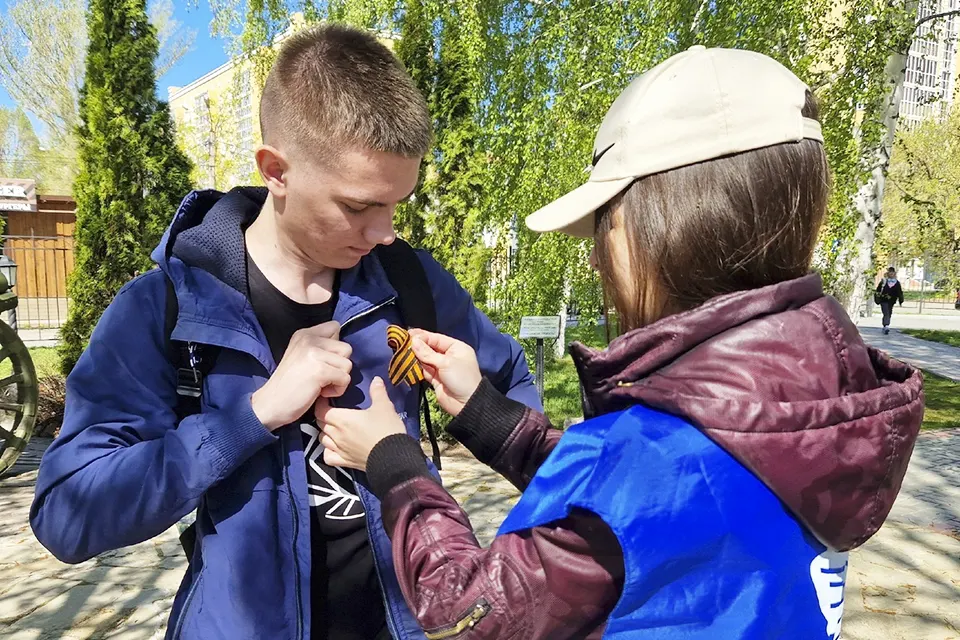 молодой человек прикрепляет георгиевскую ленту