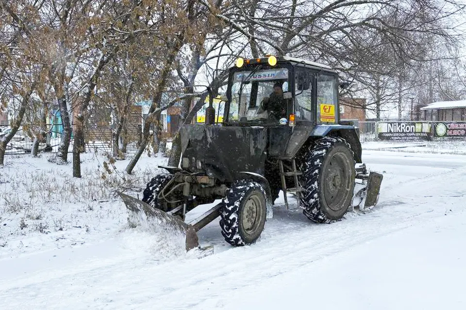 трактор убирает снег на тротуаре